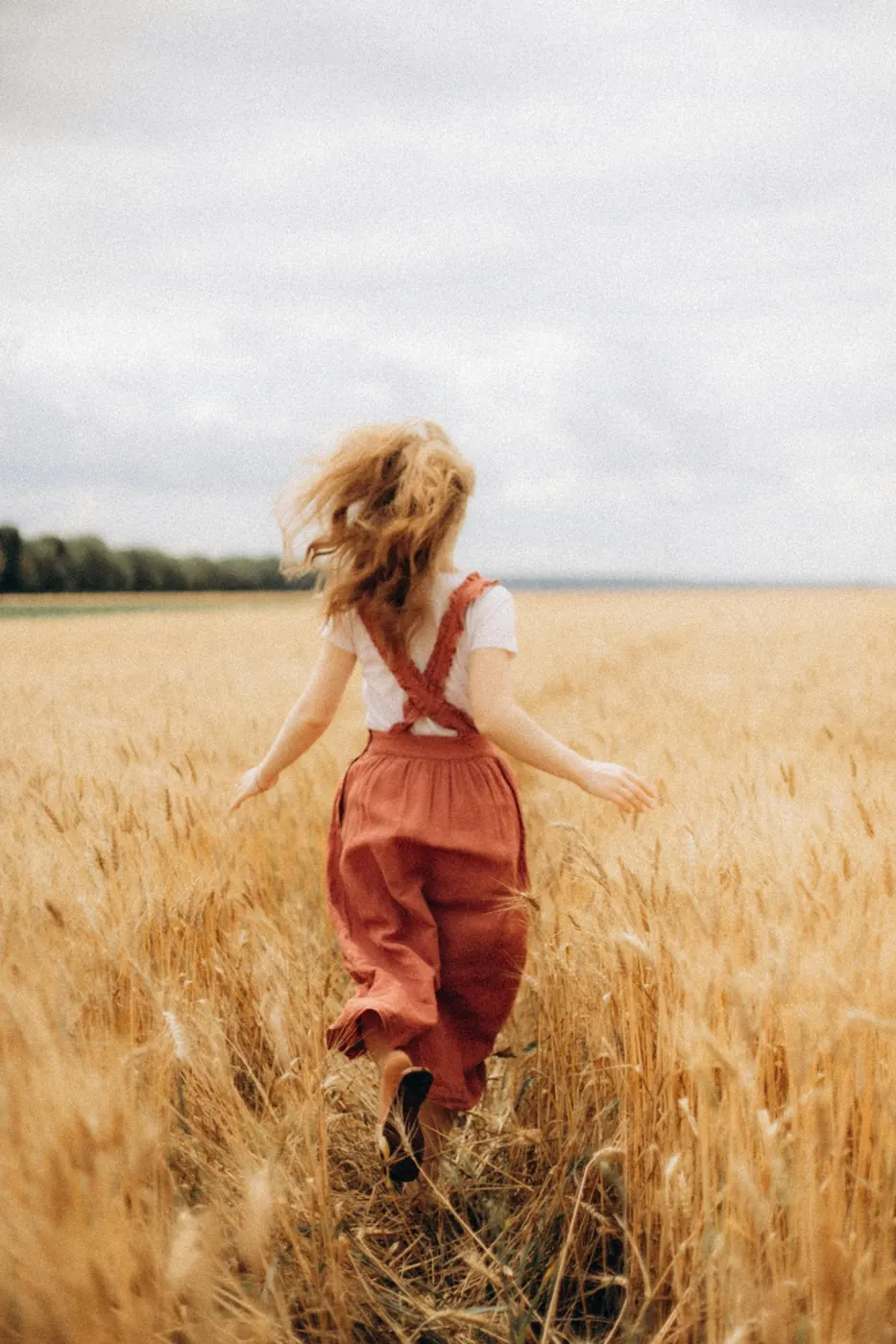 Child in a rust jumpsuit running through a wheat field